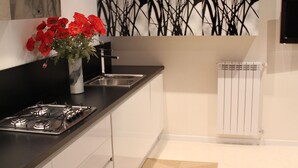 A modern kitchen with a gas stove, white cabinets, a black countertop, a vase with red flowers, and a decorative wall art piece.