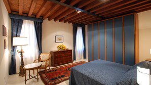 A bedroom with a wooden ceiling, a bed with a blue bedspread, a dresser, a chair, and a rug.