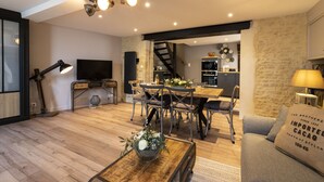 A modern living room with a wooden floor, a dining area with a table and chairs, a TV, and a staircase leading to an upper level.