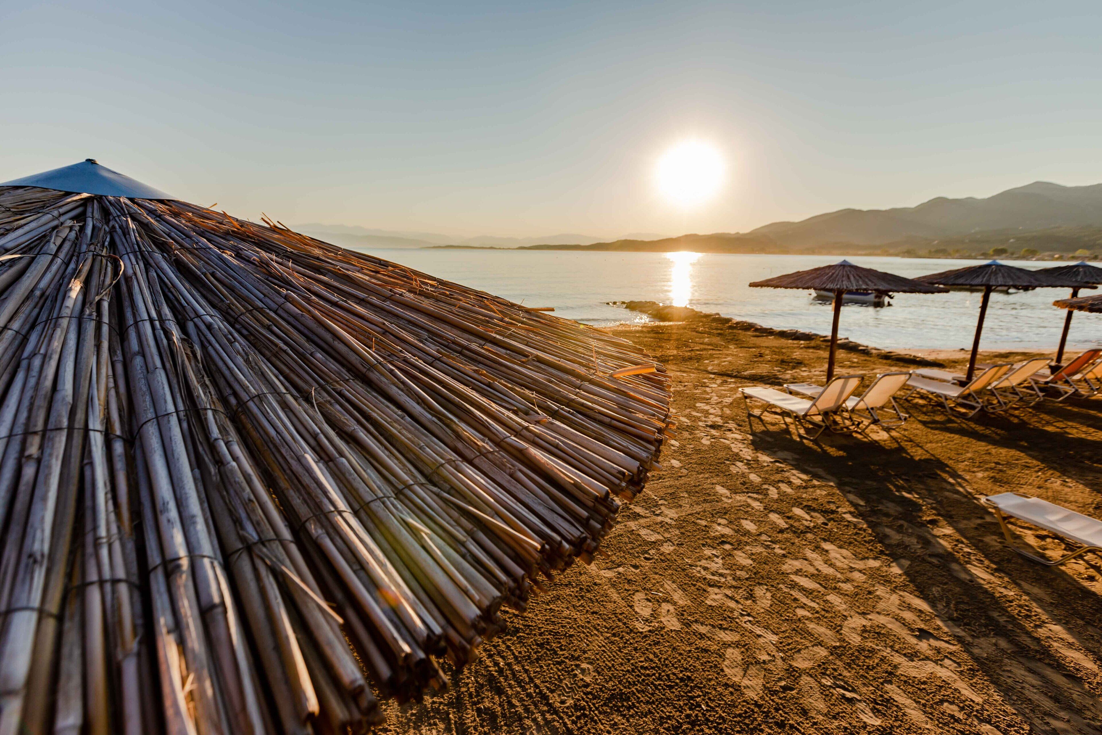 Une plage avec des parasols en bambou et des chaises longues.