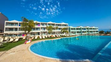 A hotel with a large swimming pool, sun loungers, and umbrellas.