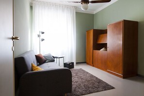 A room with a grey sofa, a wooden wardrobe, a ceiling fan, and a floor lamp. - UR NEST Borgo San Pietro (Bologna)