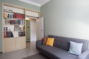 Un salon avec un canapé gris, une bibliothèque et une porte donnant sur une autre pièce.