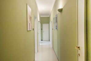 Un couloir aux murs verts, aux portes blanches et aux murs ornés de tableaux encadrés.