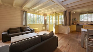 A cozy cabin interior with a wooden floor, a sofa, a dining table, and a kitchen area with a sink and stove. - Pretty family home aux Americains, spa option (CAP FERRET)