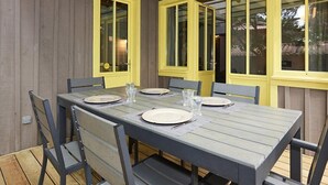 A dining table with four chairs, yellow-framed windows, and a wooden deck. - Pretty family home aux Americains, spa option (CAP FERRET)