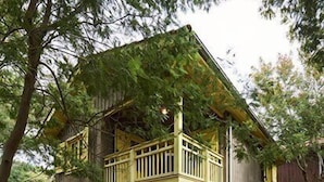 A wooden deck with a barbecue grill, outdoor seating, and a two-story house with a balcony. - Pretty family home aux Americains, spa option (CAP FERRET)