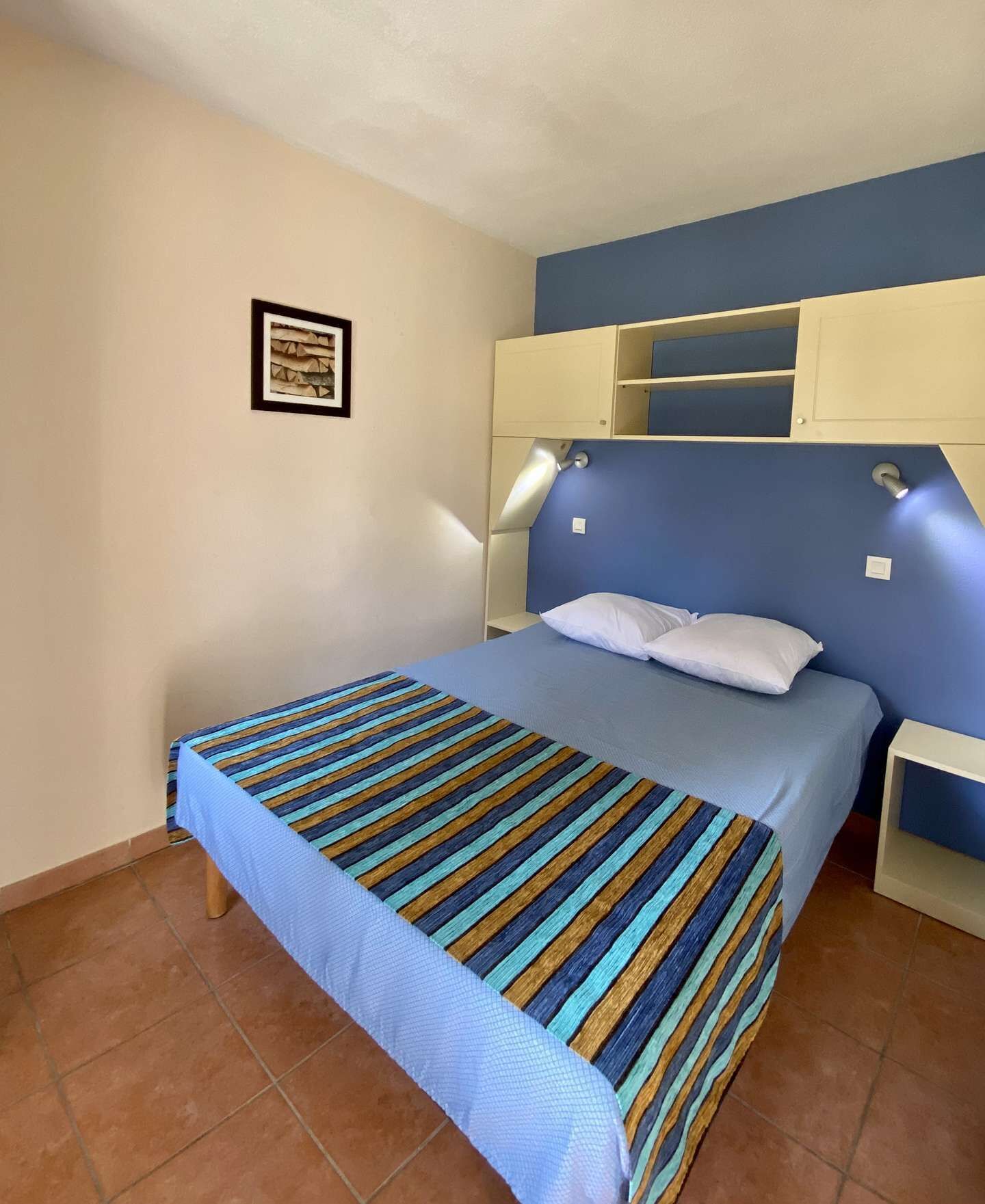 Una camera da letto con un letto, un comodino, una mensola a muro e un quadro incorniciato.