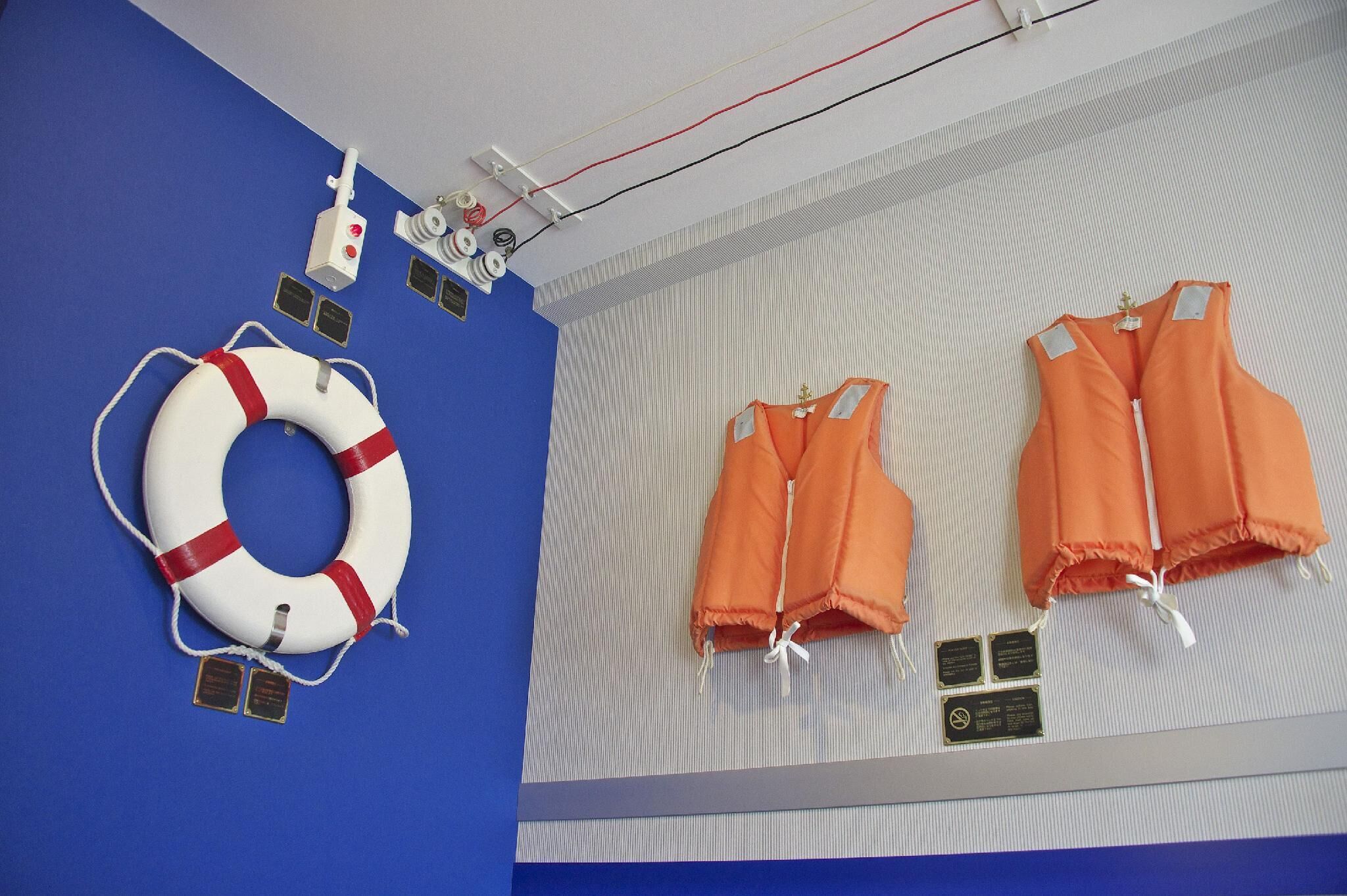 A blue wall with a white lifebuoy and orange life jackets displayed.