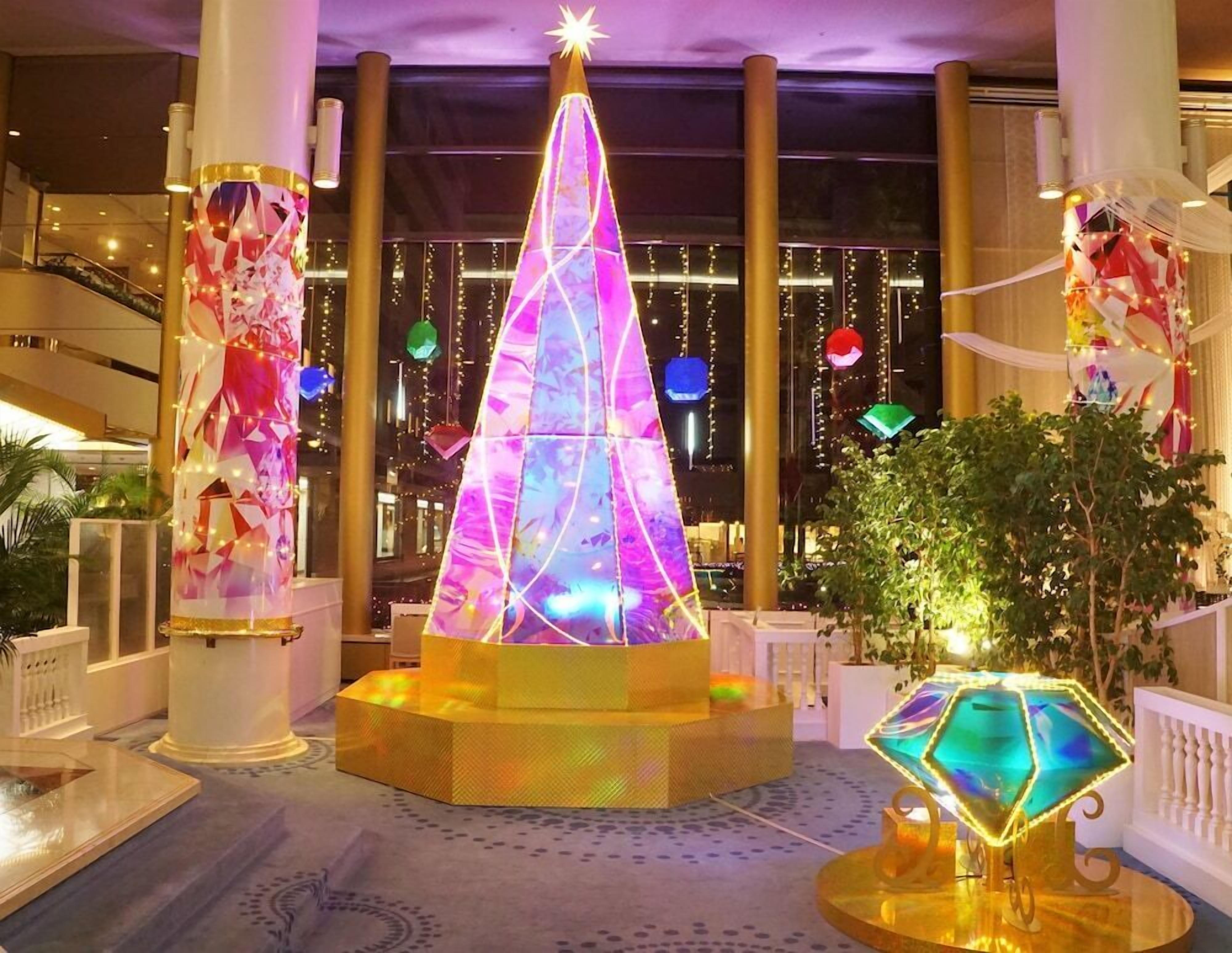 A lobby with a large, illuminated Christmas tree, a grand staircase, and a decorative fountain.