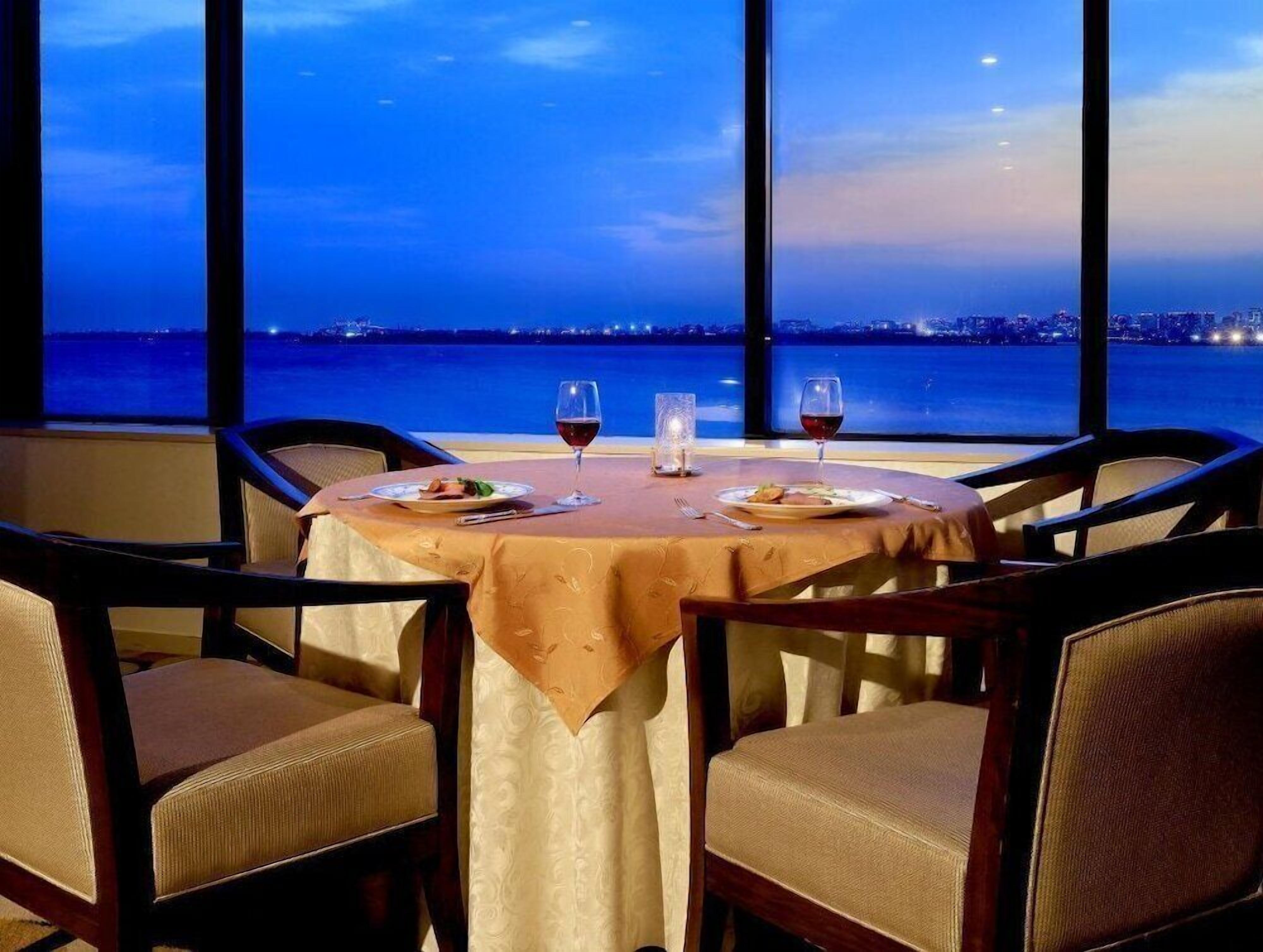 Uma mesa posta para dois com vista para o mar e luzes da cidade ao entardecer.
