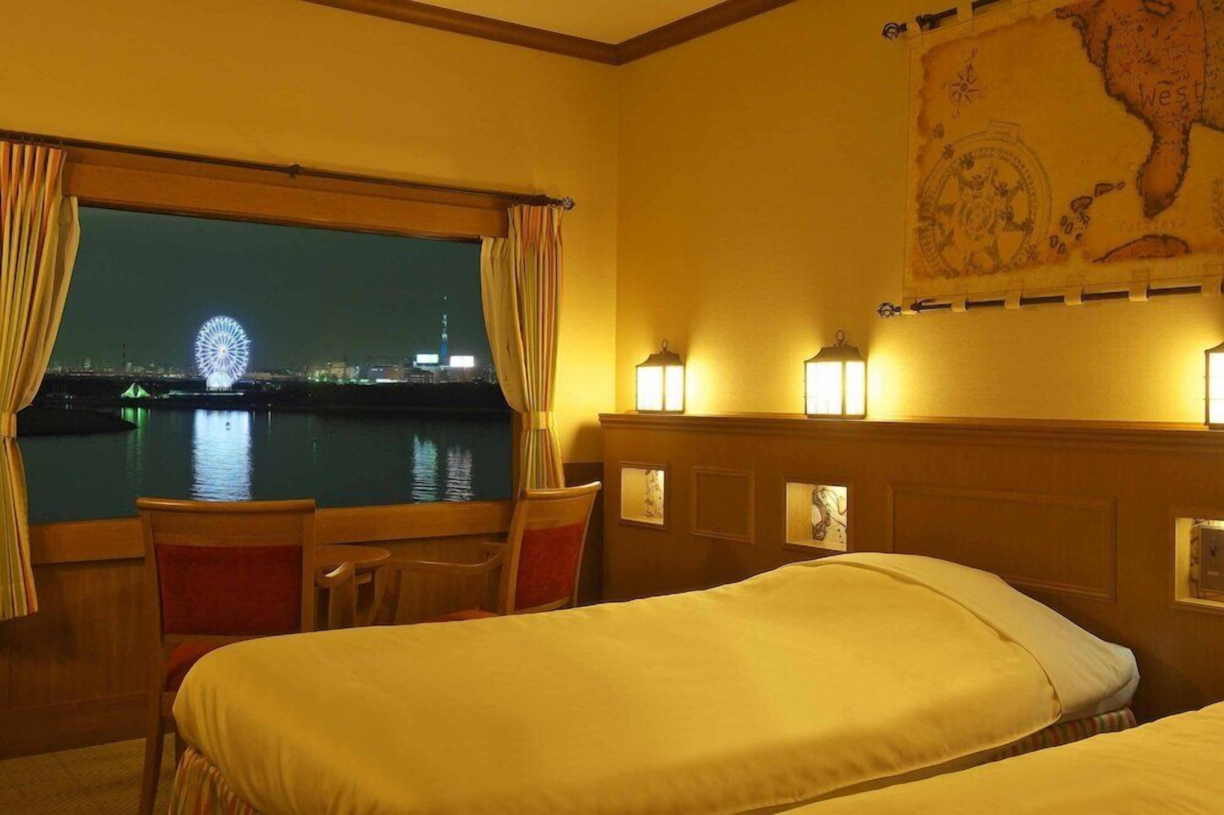 Quarto de hotel com duas camas, vista para uma roda-gigante à noite, um mapa na parede e uma janela com cortinas.