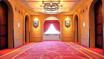 A hotel hallway with a red carpet, arched doorways, and a chandelier.