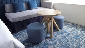 A modern hotel room with a grey sofa, blue cushions, a round wooden table, and matching ottomans. - Tokyo Bay Maihama Hotel First Resort (Urayasu)