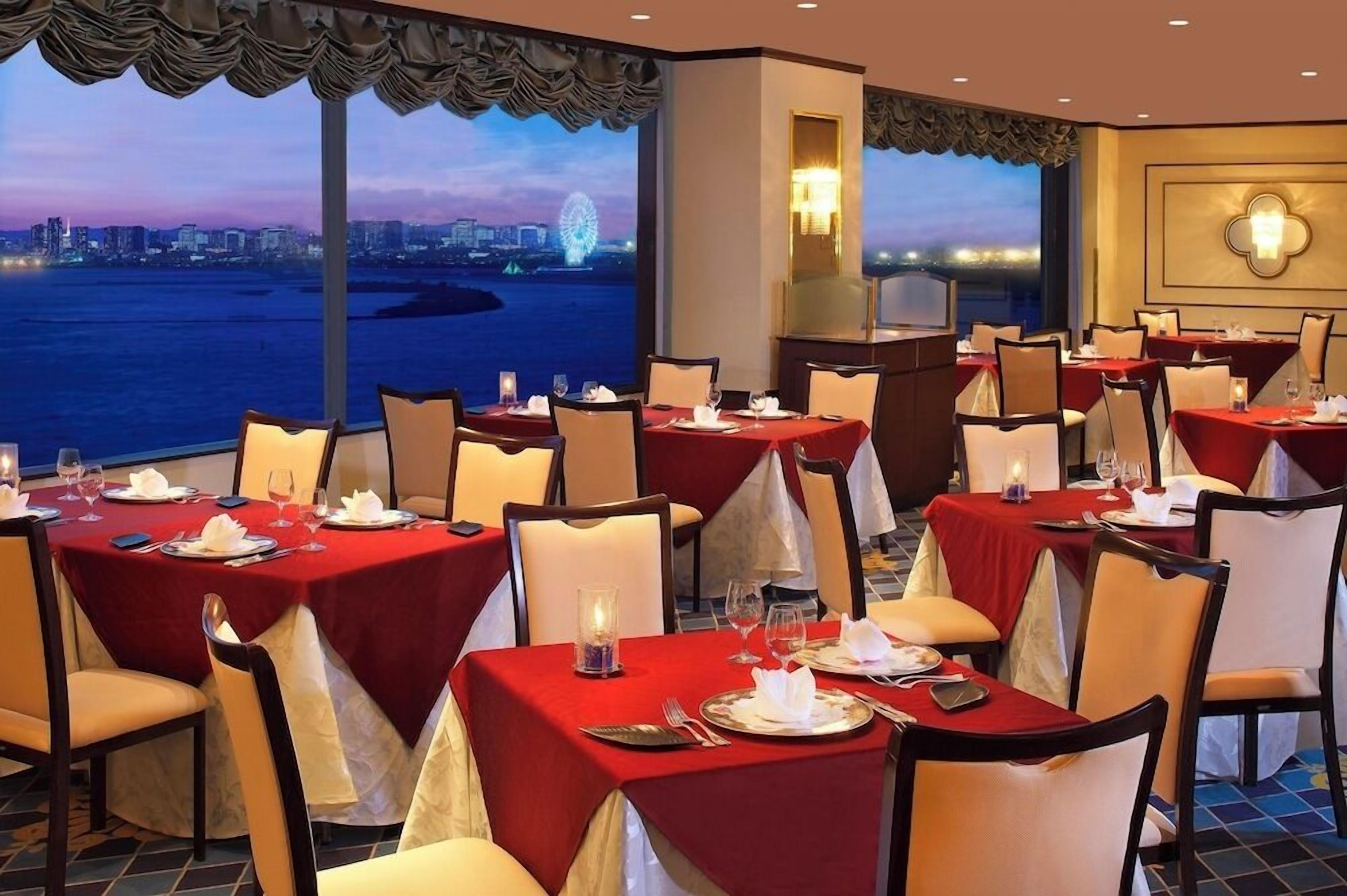 A restaurant with tables set for dining, large windows with a city view, and a decorative wall light.