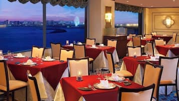 A restaurant with tables set for dining, large windows with a city view, and a decorative wall light.
