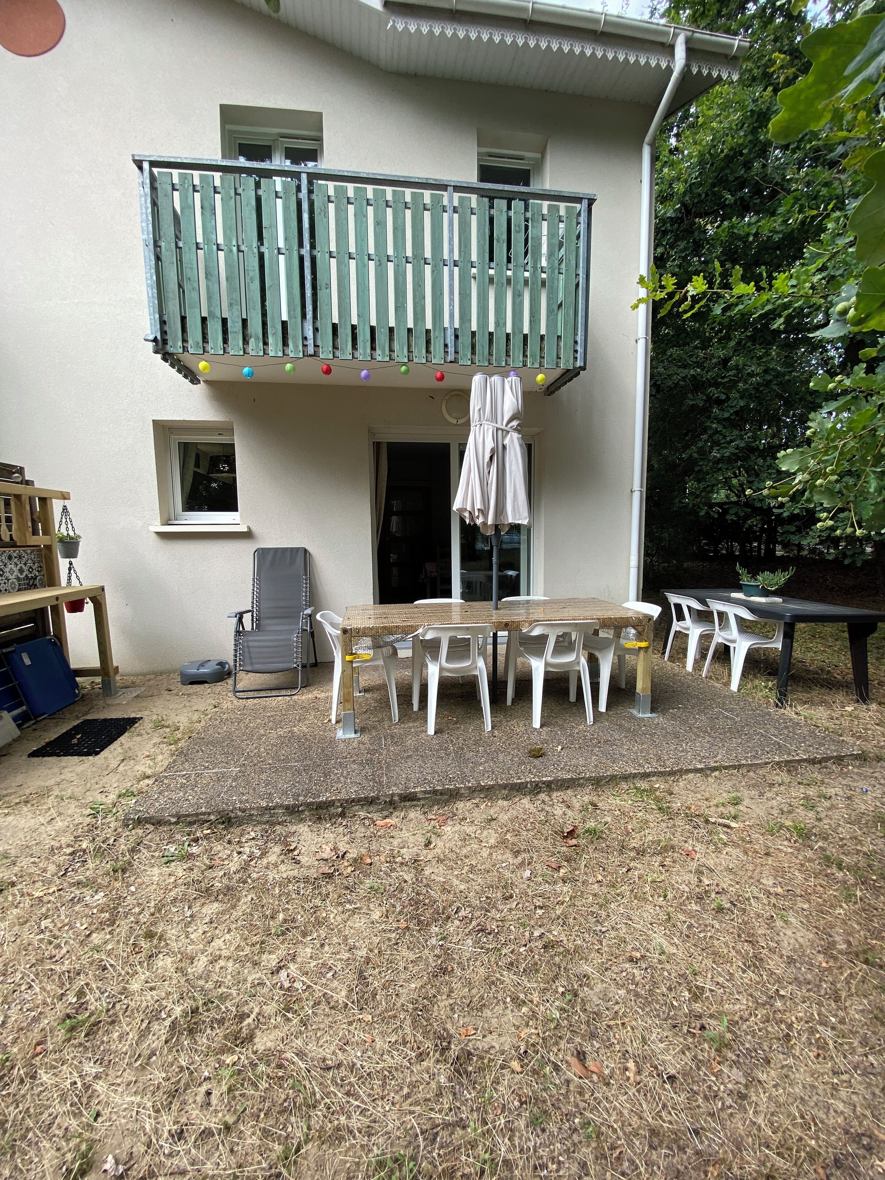 A two-story building with a balcony, a table with chairs, and a small garden area.