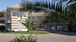 A building with a tiled roof, striped facade, and a paved courtyard with palm trees.