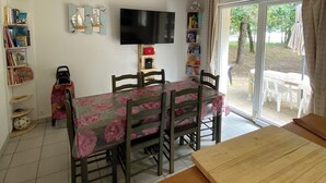 A dining area with a table set for four, a television mounted on the wall, and a bookshelf filled with books and decorative items.
