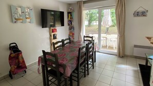 A dining area with a table and chairs, a television on the wall, and a view of the outdoors through a glass door.