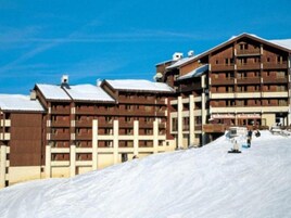 A multi-story wooden lodge with a ski slope in the background.