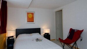 A bedroom with a bed, two bedside tables, a red chair, a door, and a wall with a framed picture. - Residence Le Cervin (La Plagne-Tarentaise)