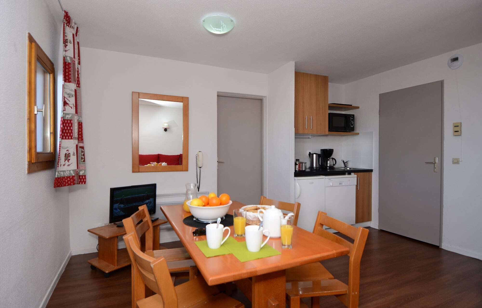 A dining area with a wooden table and chairs, a breakfast setup with orange juice and a bowl of fruit, a microwave, and a coffee maker in the kitchen area.