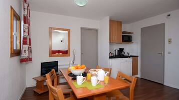 A dining area with a wooden table and chairs, a breakfast setup with orange juice and a bowl of fruit, a microwave, and a coffee maker in the kitchen area.
