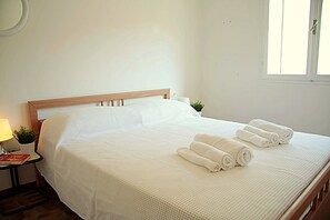 A neatly made bed with white linens and rolled towels, a bedside lamp, and a small potted plant on the nightstand. - Pasubio 1 - Three-bedroom apartment with air conditioning near the ocean. (Comacchio)