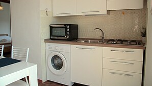 Ett kompakt kök med tvättmaskin, mikrovågsugn och gasspis.