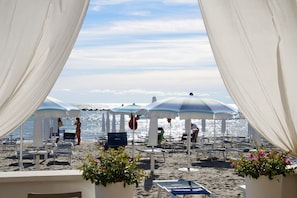A beach with white canopies and lounge chairs, a clear sky, and the ocean in the background. - Pasubio 1 - Three-bedroom apartment with air conditioning near the ocean. (Comacchio)