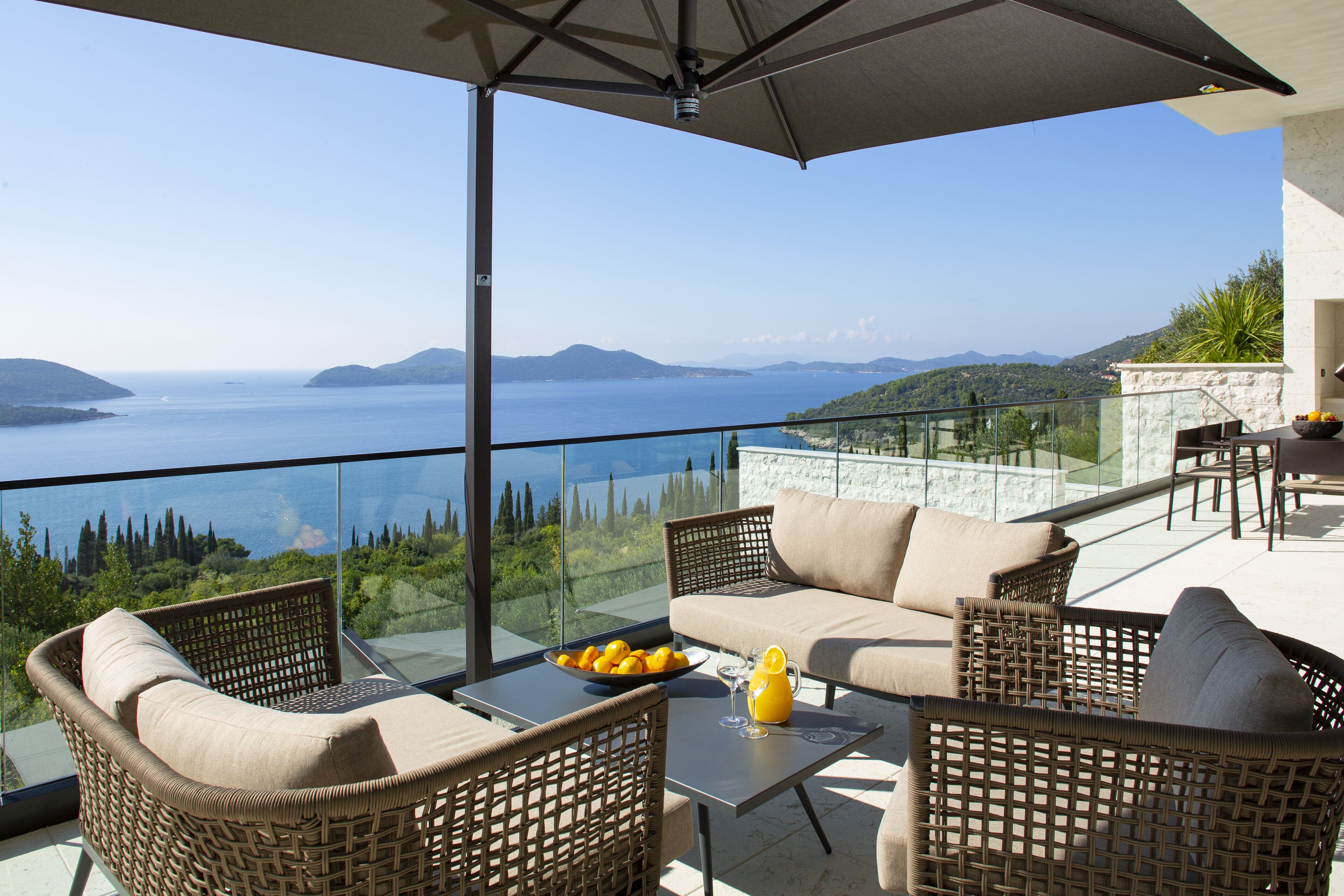 A balcony with wicker furniture, a glass table, and a bowl of fruit.