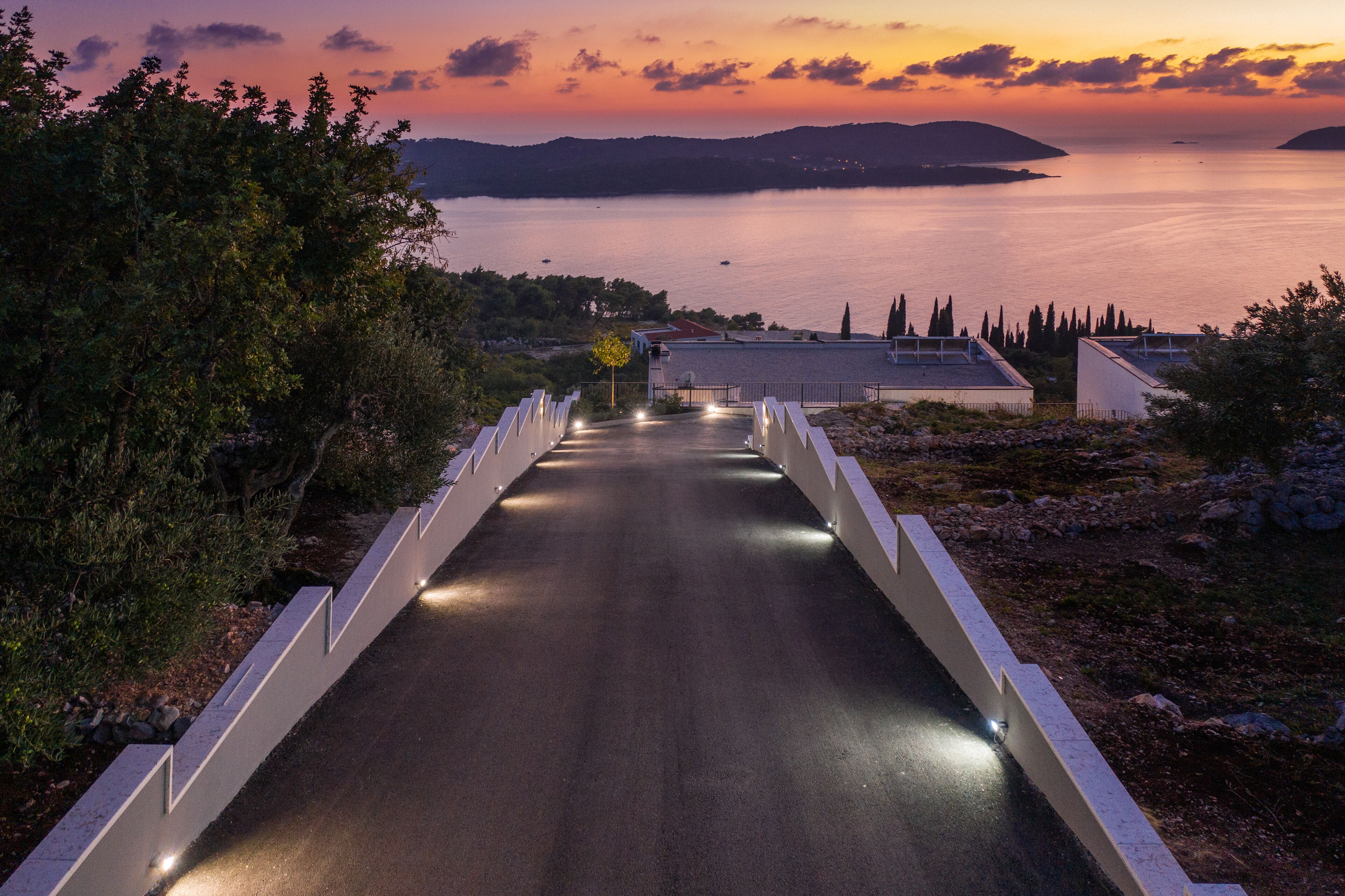 A road leading to a coastal area with a view of the sea and hills in the distance.