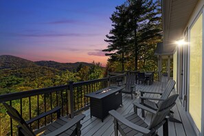 Terraza con mobiliario exterior y una chimenea, con vistas a un paisaje boscoso.