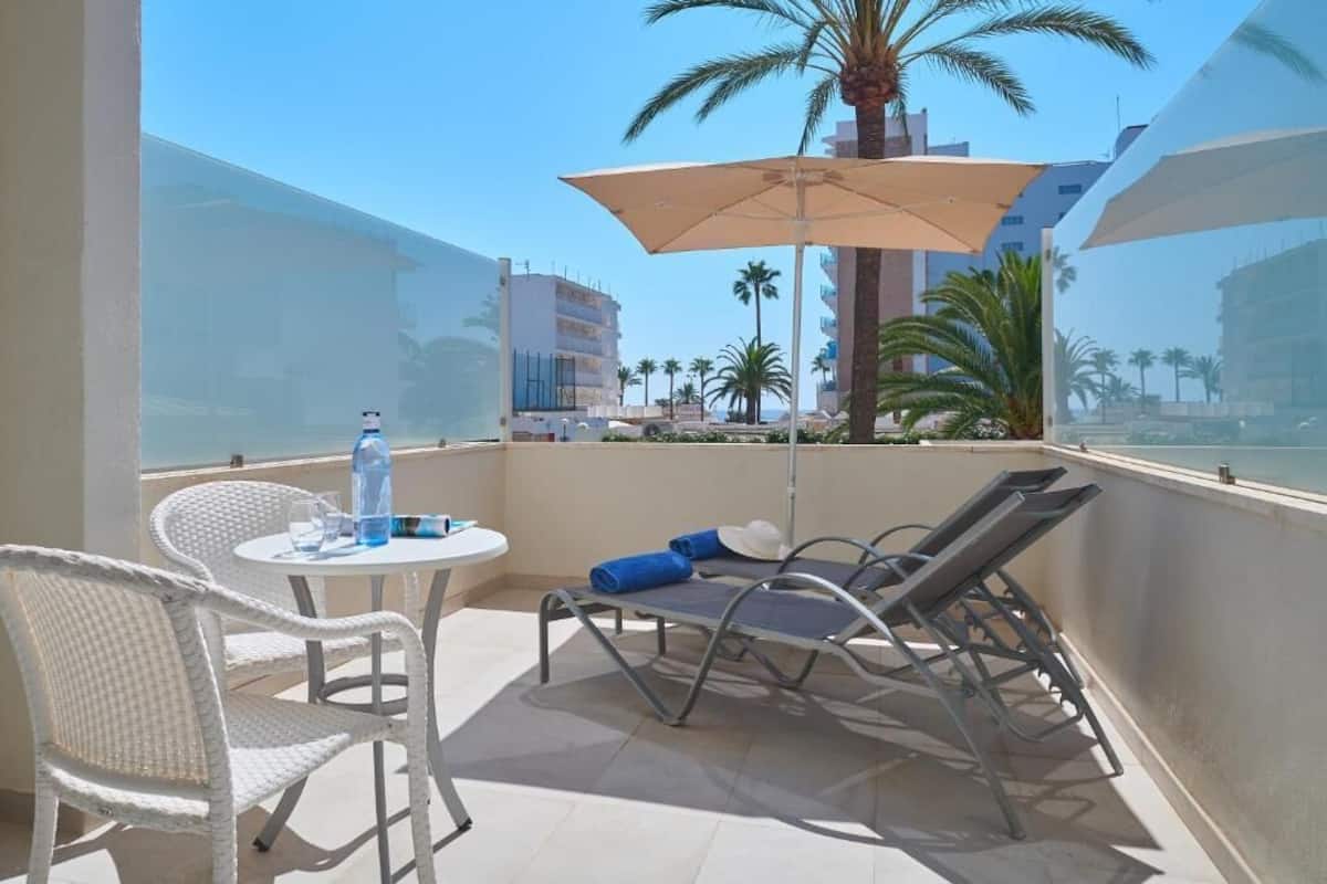 A balcony with a table, chairs, and a sun umbrella.