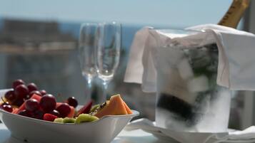 En skål med frukt, ett glas vatten och en flaska champagne står på ett bord med utsikt över staden.