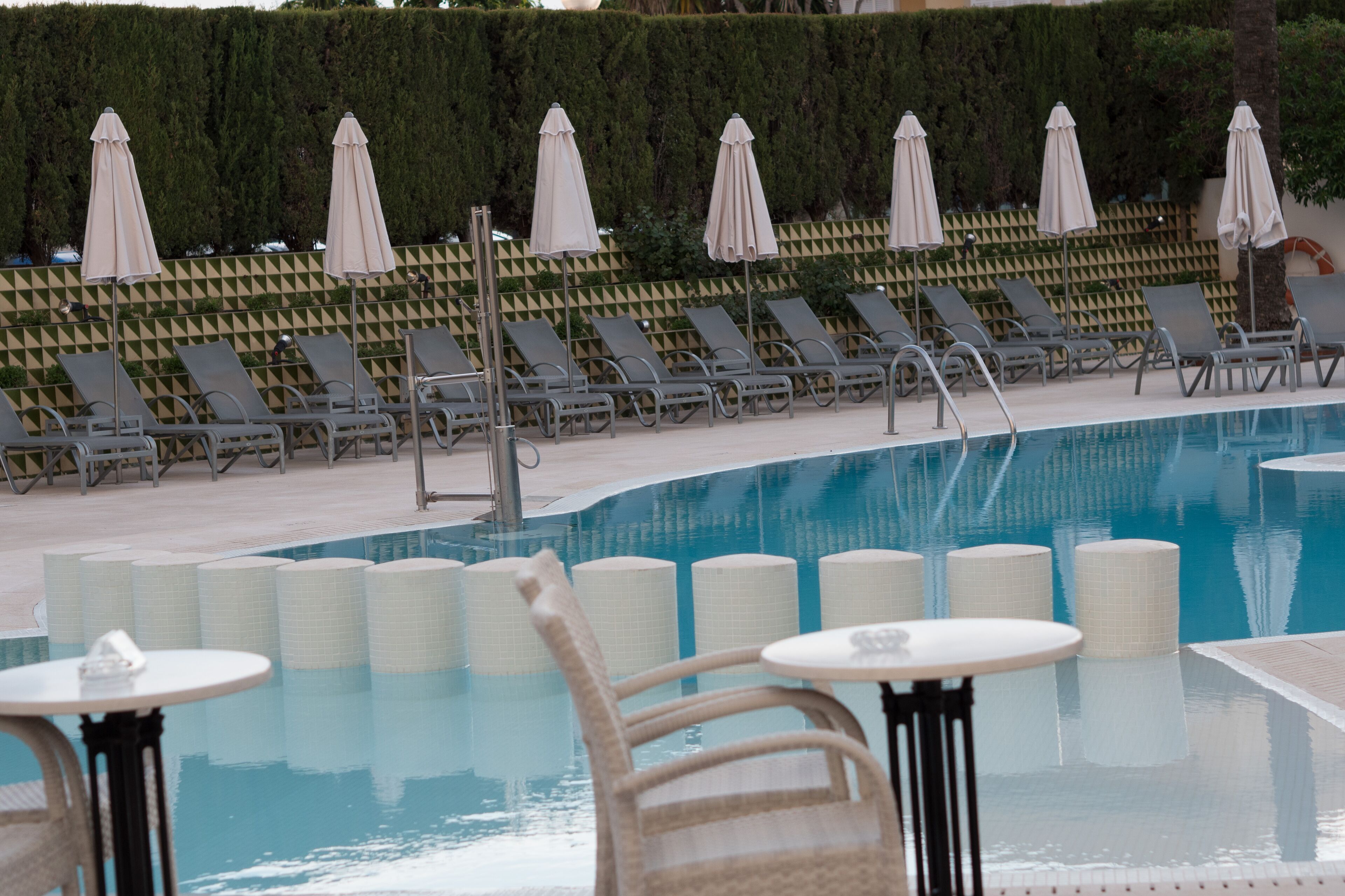 Zona de piscina con sillas de descanso y sombrillas, un deck con baldosas y una piscina cristalina.