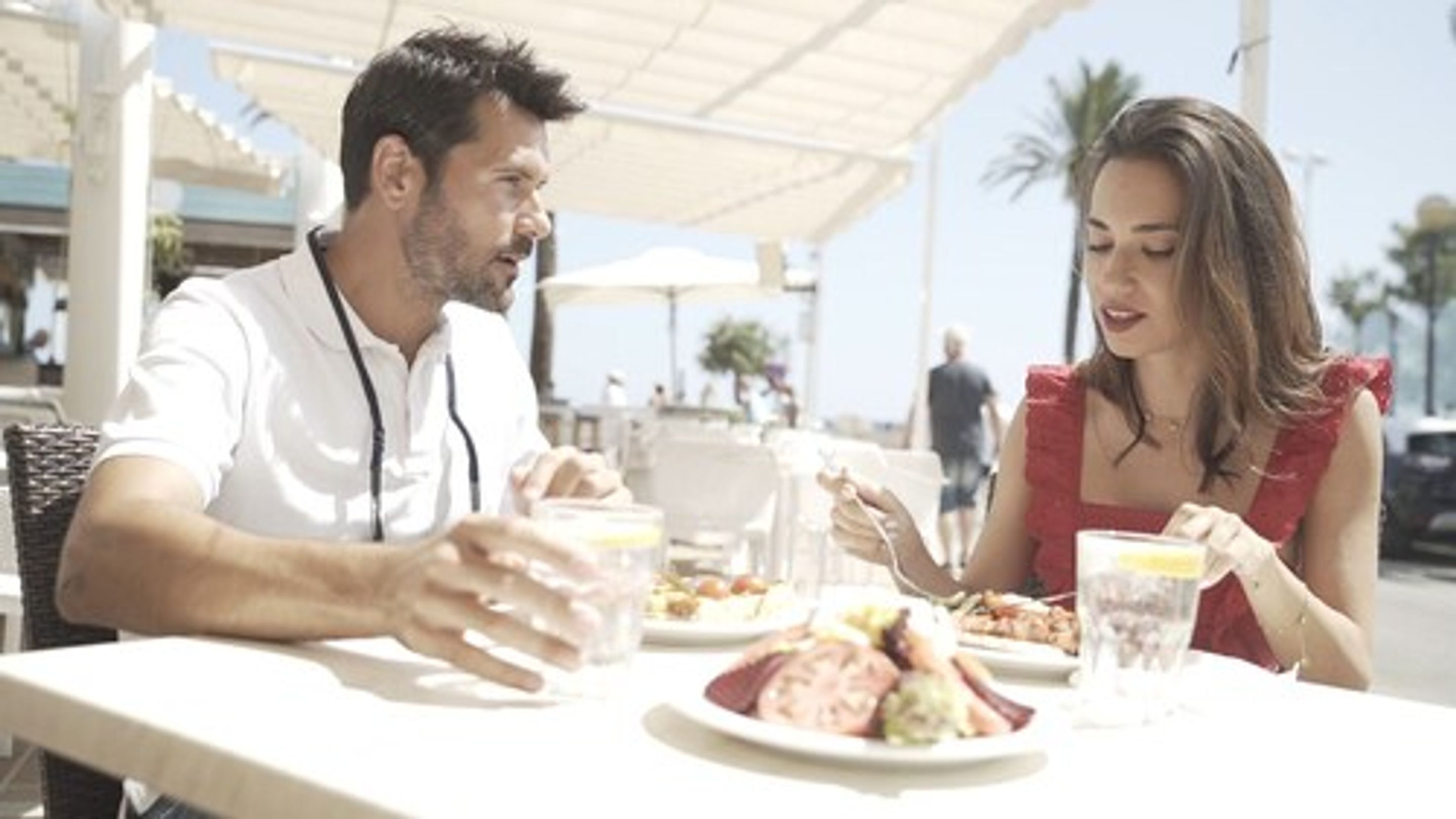 A couple dining at an outdoor restaurant with a view of palm trees and a clear sky.