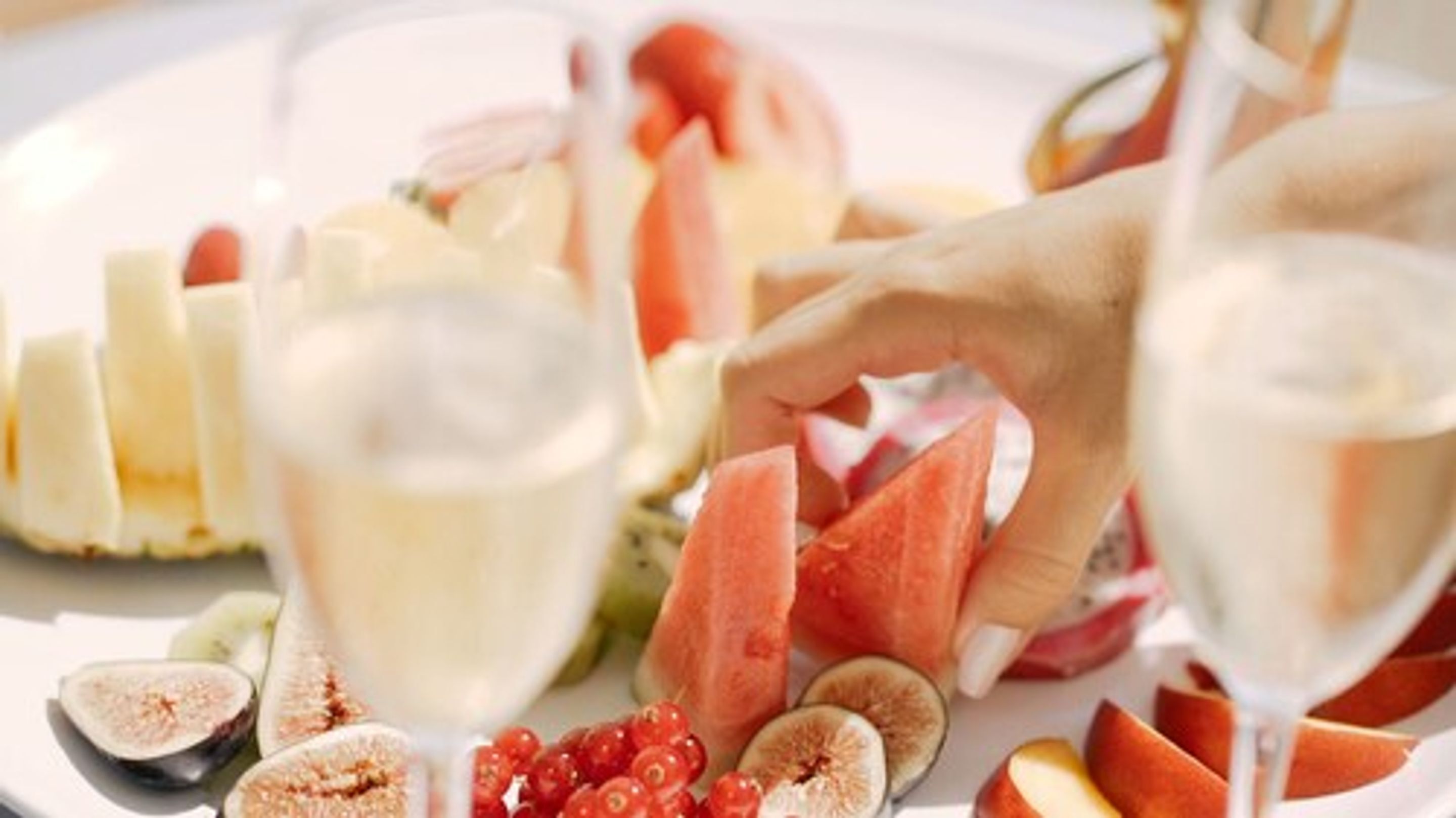 A plate of assorted fruits and cheeses with a hand reaching for a piece.