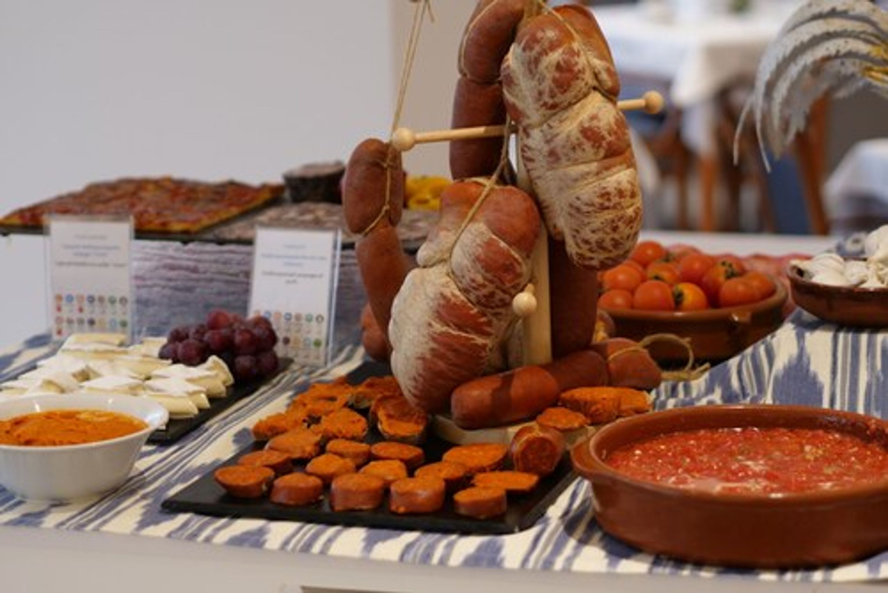 Un bufé con distintos tipos de comida, incluyendo salchichas, quesos y un tazón de salsa roja.