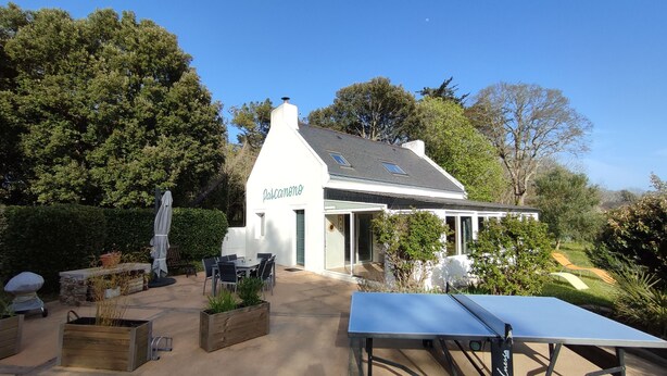 A white building with a sign reading "Pascano" in a garden setting with outdoor seating and a ping pong table. - Logement Locatif à Belle-ile : Maison Avec Jardin Partagé (Le Palais)