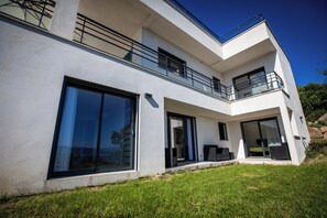 Ett modernt hus i två våningar med stora skjutbara glasdörrar, en balkong och en välskött gräsmatta.