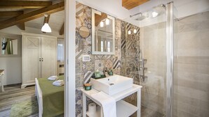 Ein Badezimmer mit Dusche, Waschbecken und Spiegel. Ein Handtuch liegt auf dem Boden und ein grünes Handtuch auf dem Bett.