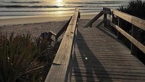 Een houten looppad dat naar een strand leidt, met een ondergaande zon op de achtergrond.