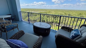 Een balkon met rieten meubilair, een ronde tafel en uitzicht op een groen landschap.