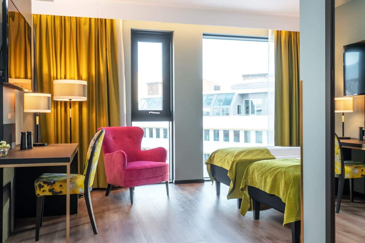 Quarto de hotel com escrivaninha, cadeira, cama e televisão.