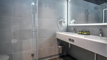 A modern bathroom with a glass shower enclosure, a white sink with a mirror, and a trash bin.