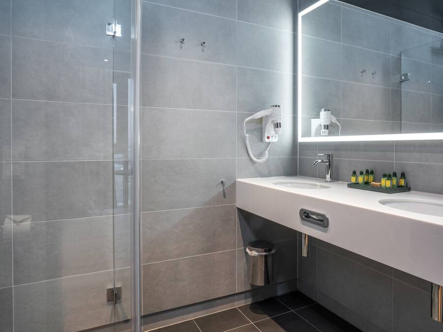 A modern bathroom with a glass shower enclosure, a white sink with a mirror, and a trash bin.