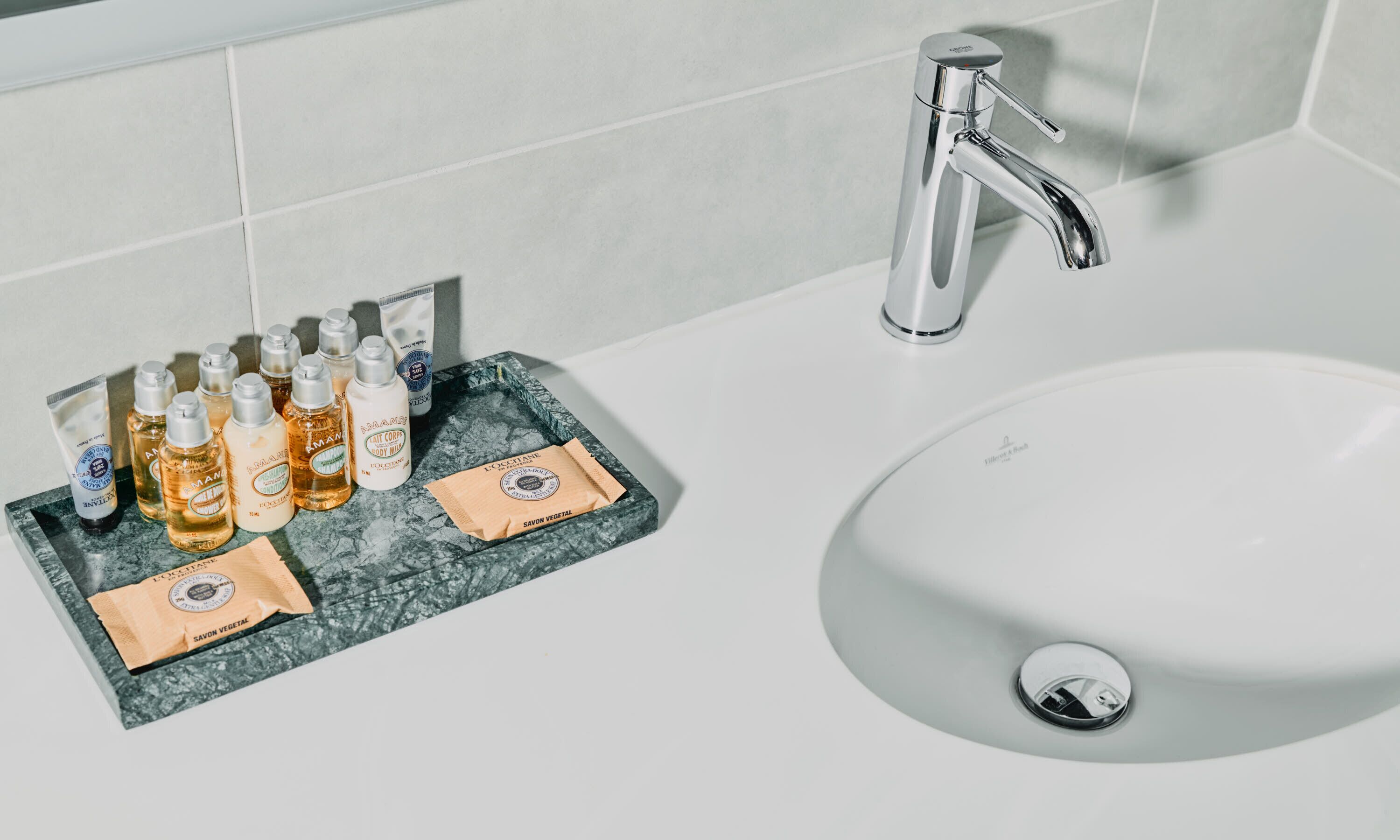 A bathroom with a white sink, a chrome faucet, and a marble tray holding toiletries.