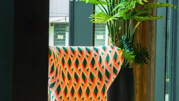 Una ventana con vista a un edificio, una planta en maceta y un sillón con estampado.